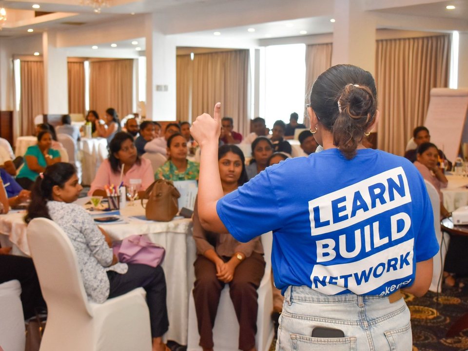 Chamathka facing a room of seated participants at round tables